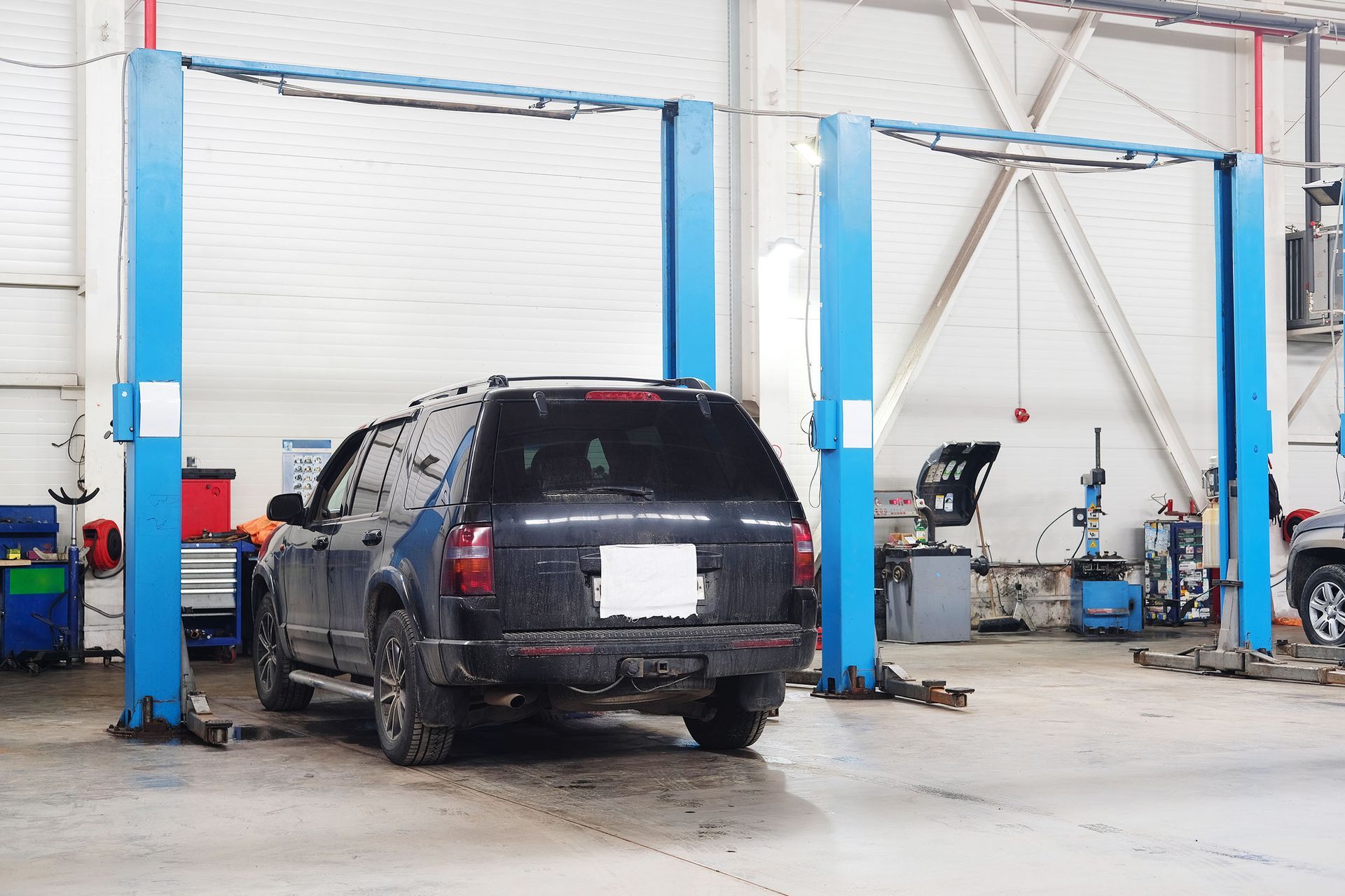 SUV in an auto repair shop lift bay, parked near blue and white hydraulic lifts.