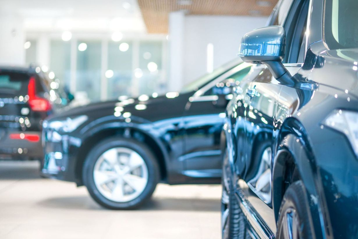 Shiny cars lined up in a bright showroom, with a black car centered and a blue car in the foreground