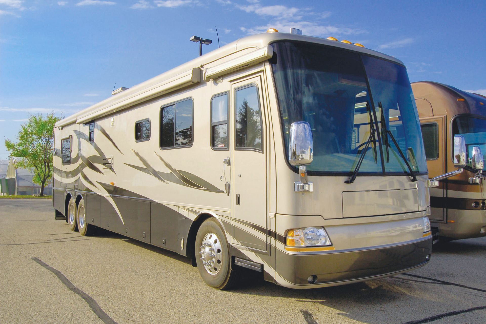White RV parked on a beach, blue water and sky in the background. Two cars are parked on either side.