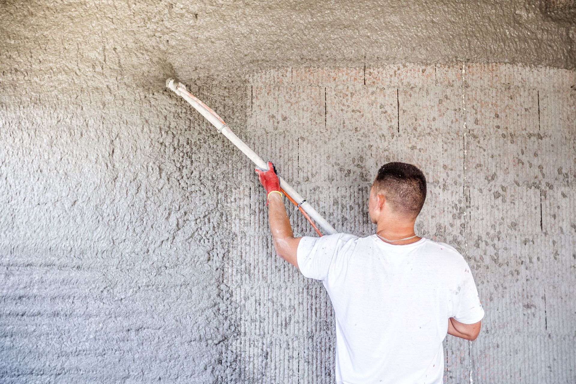 Person plastering a wall and ceiling with a long-handled tool. Interior shot.