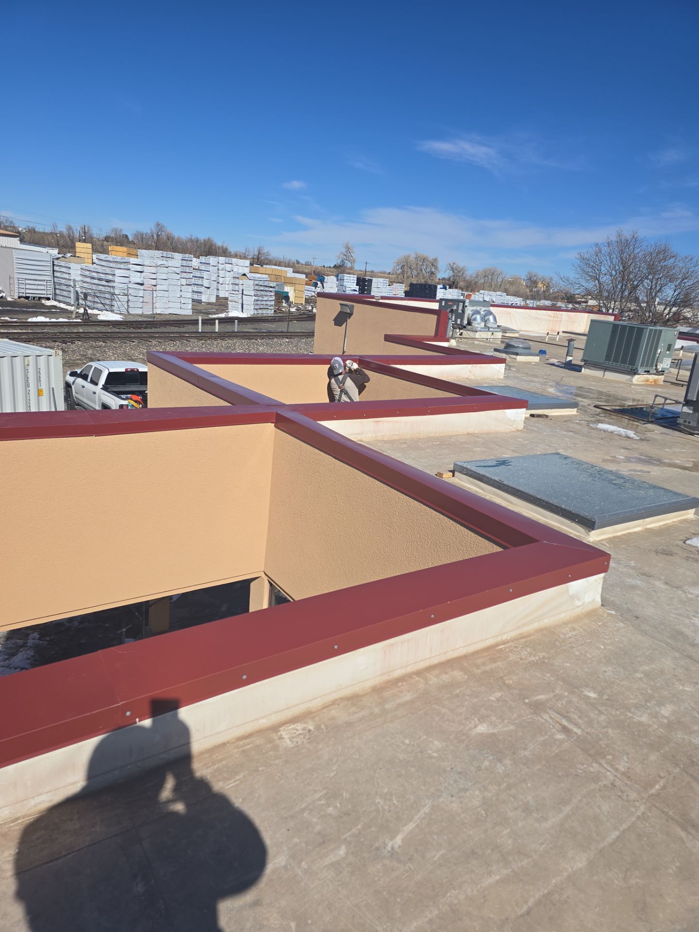 View of a flat roof with several square openings, tan walls, red trim. Bright blue sky.