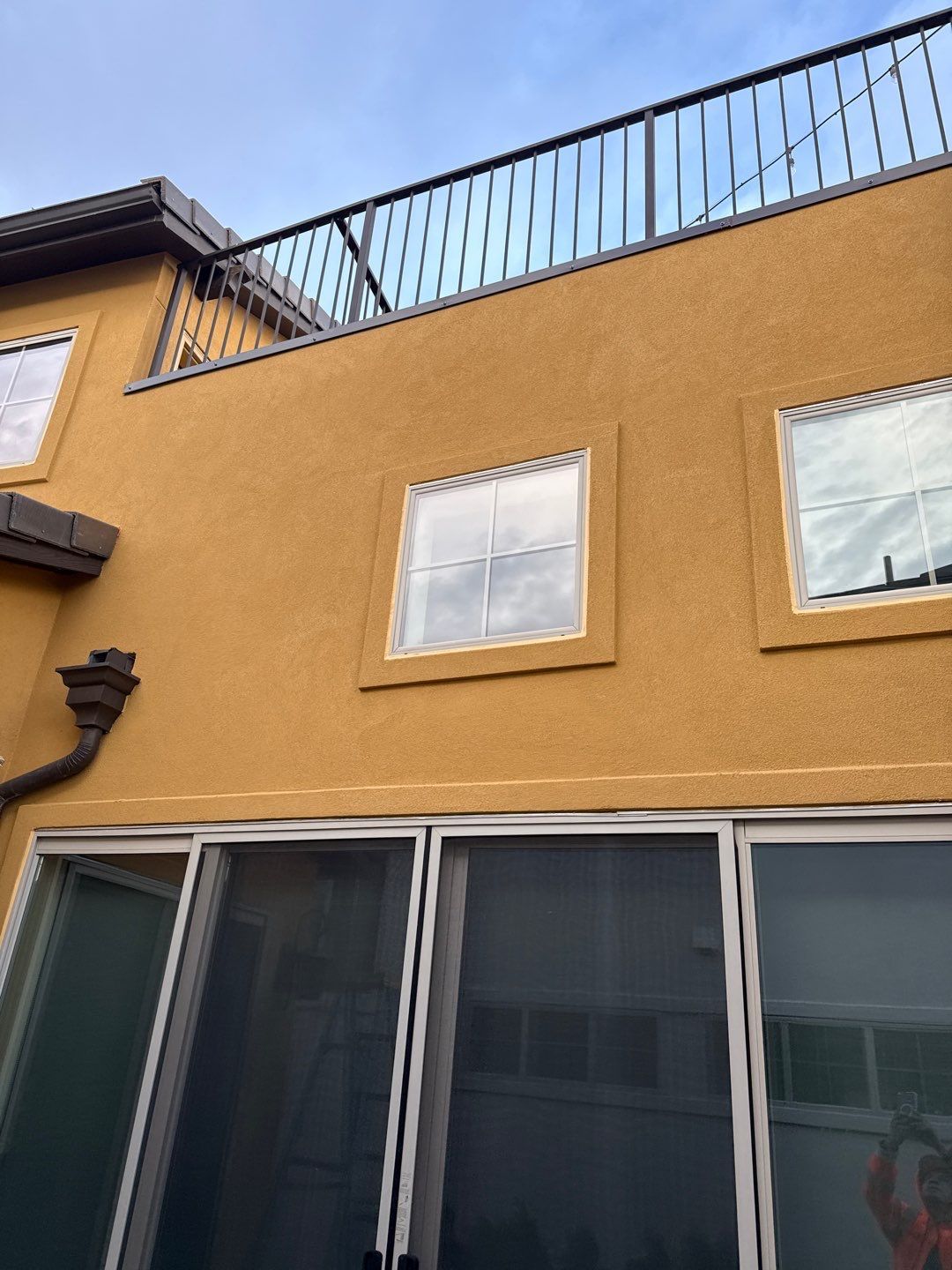 Yellow stucco building with windows and a black balcony. Brown gutter - after