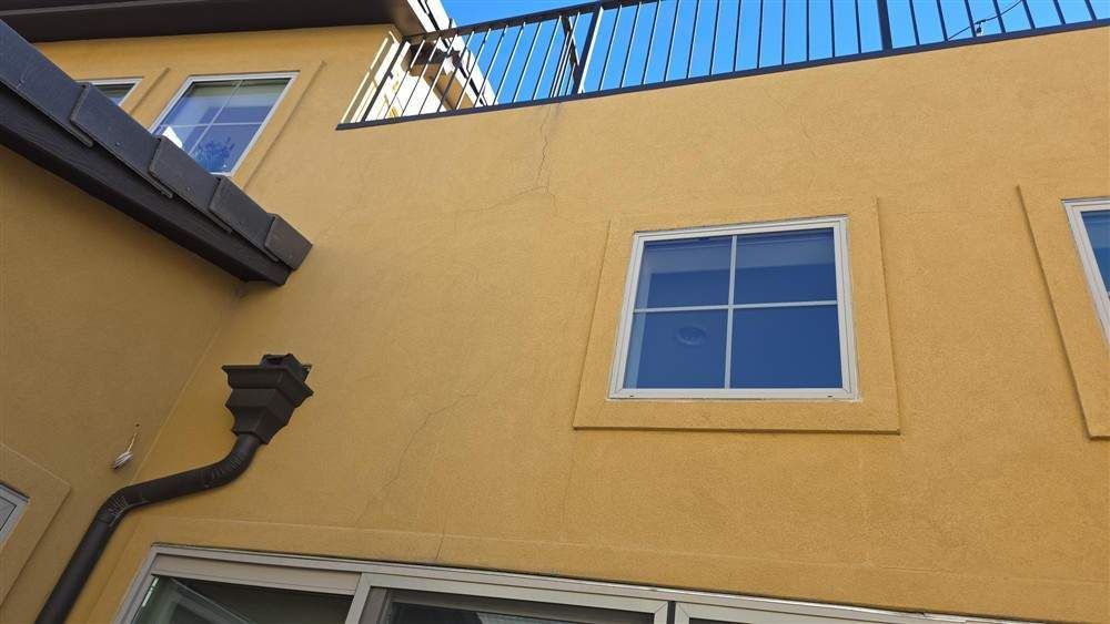 Yellow stucco building with windows and a black balcony. Brown gutter - before
