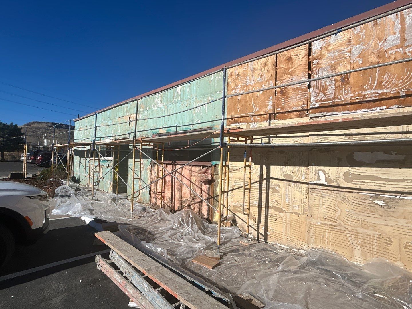 Building exterior under renovation. Scaffolding, peeling paint, and blue sky.