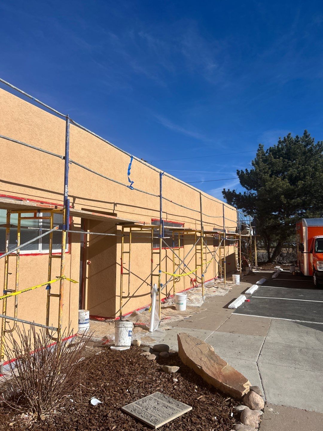 Building exterior with scaffolding for renovation work; tan stucco, blue sky.