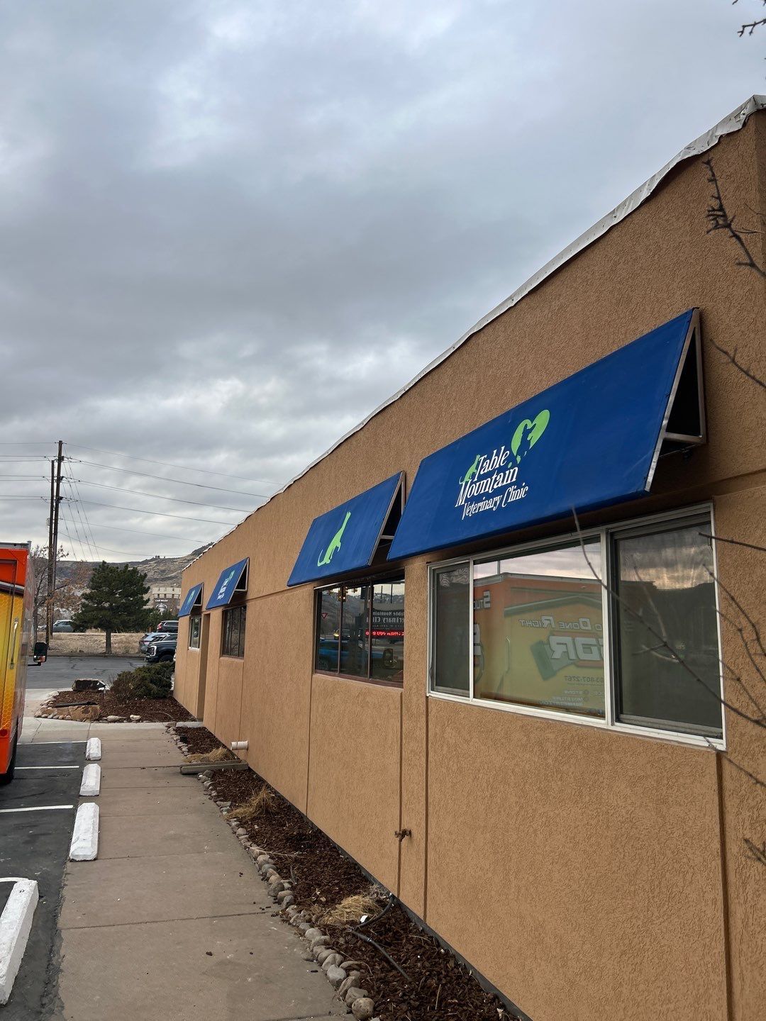 Exterior of a restaurant with blue awnings. Signage reads Olive Garden Italian Kitchen. Beige building, cloudy sky.