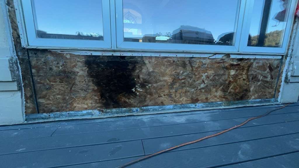 Damaged exterior wall under a window, showing water damage, on a deck with an electric cable. 