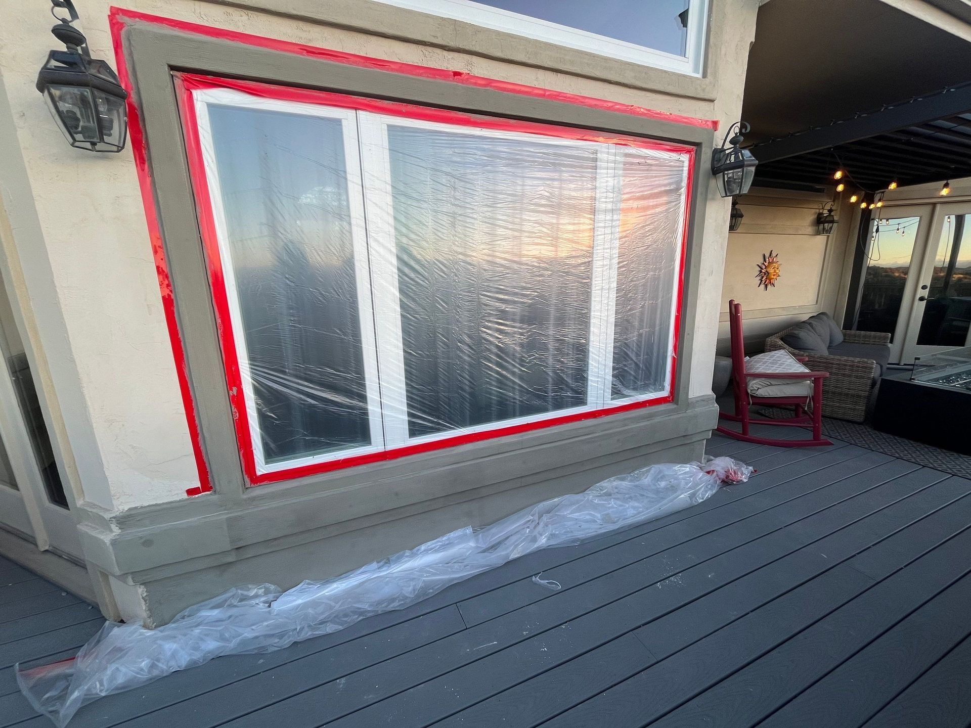Window covered with plastic for protection, red tape outlining frame. Exterior view on a deck. 