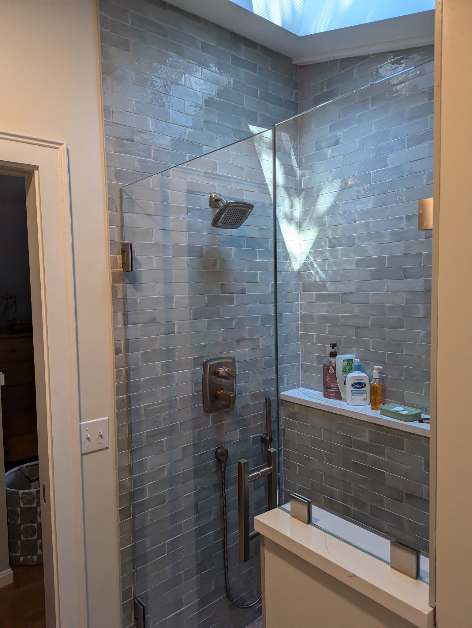 A bathroom with a walk in shower with a skylight above it.