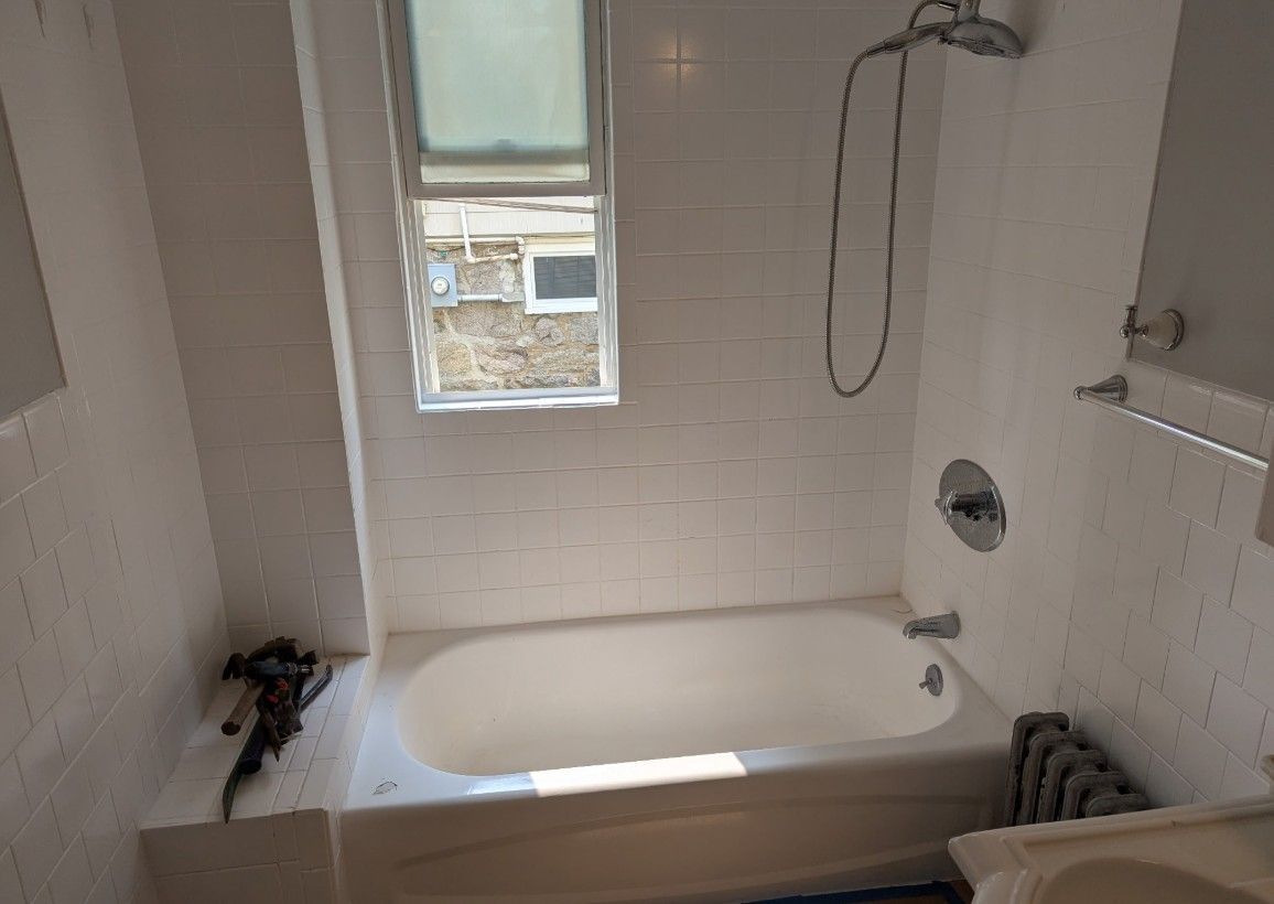 White tiled bathroom with a bathtub, showerhead, and small window.