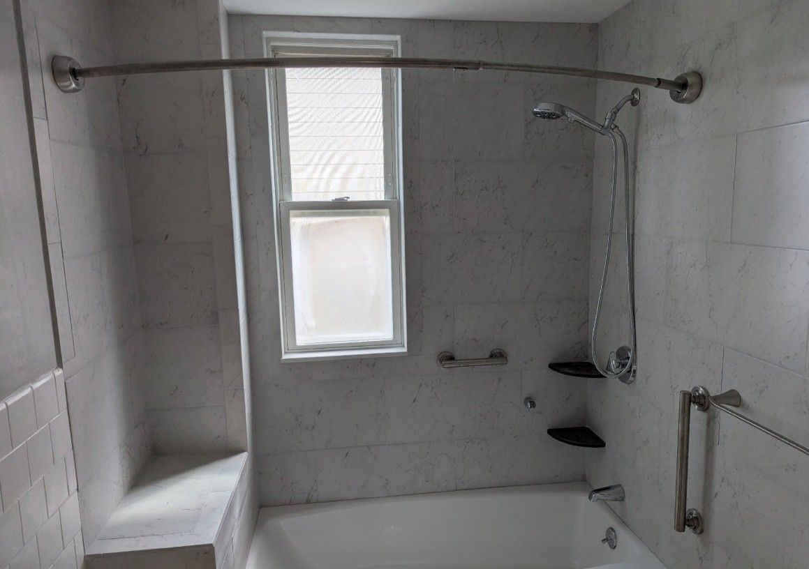 Bathroom with white tile, a tub, shower, and a window.