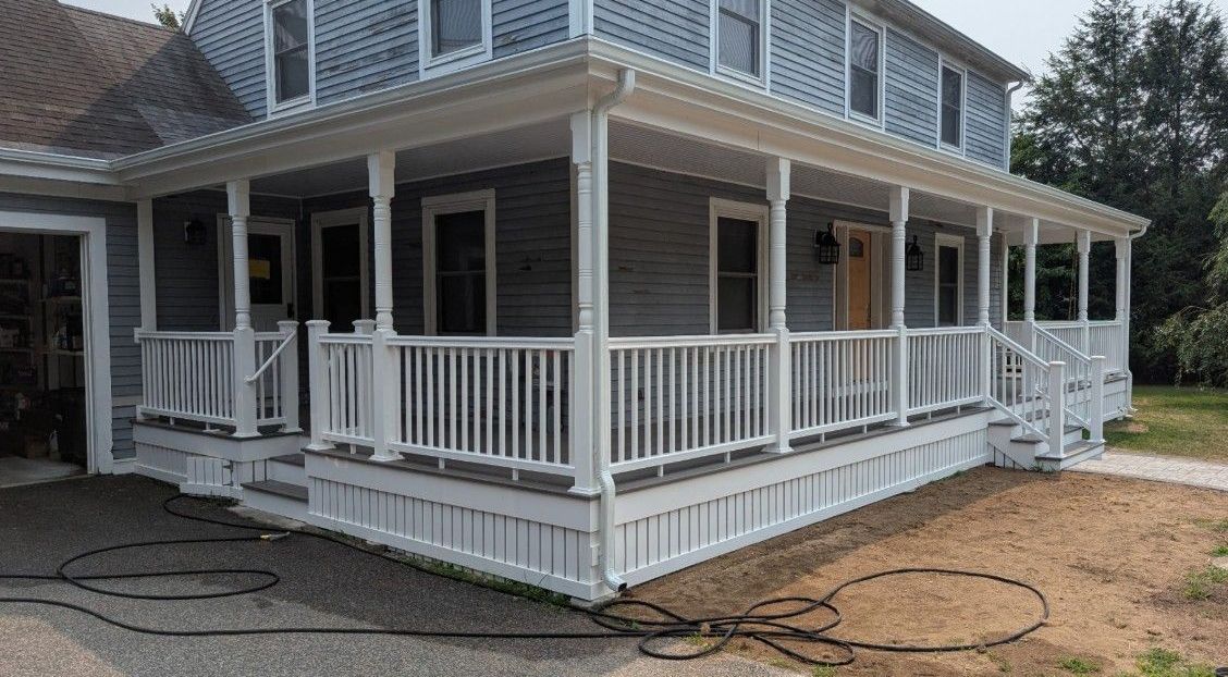 Two-story grey house with white wraparound porch and railing.