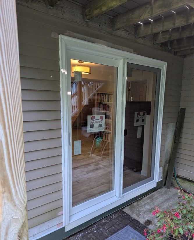 Sliding glass door with white frame on a beige house exterior. The door is open, revealing a well-lit interior.