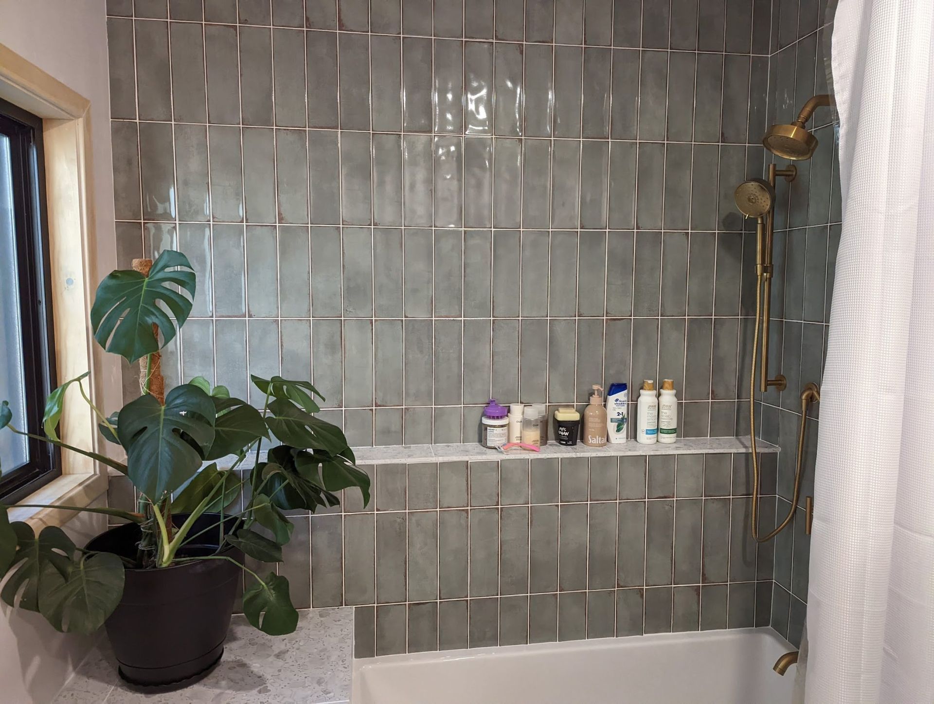 A bathroom with a shower, tub, shelf and window.