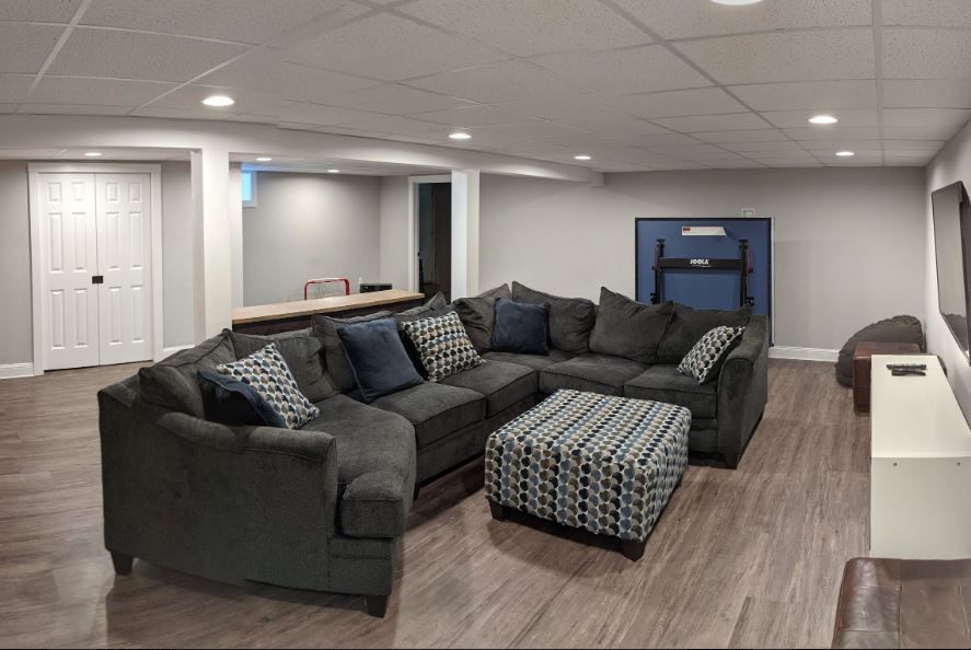A living room in a basement with a large sectional couch and ottoman.