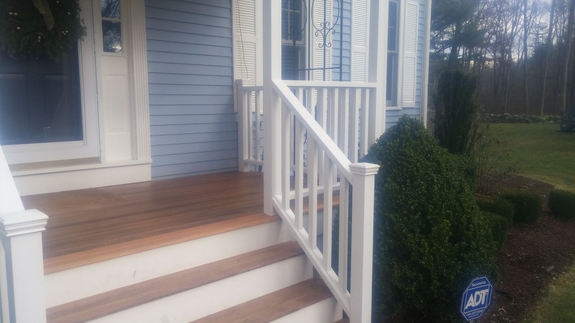 A white porch with wooden steps and a white railing on a blue house.