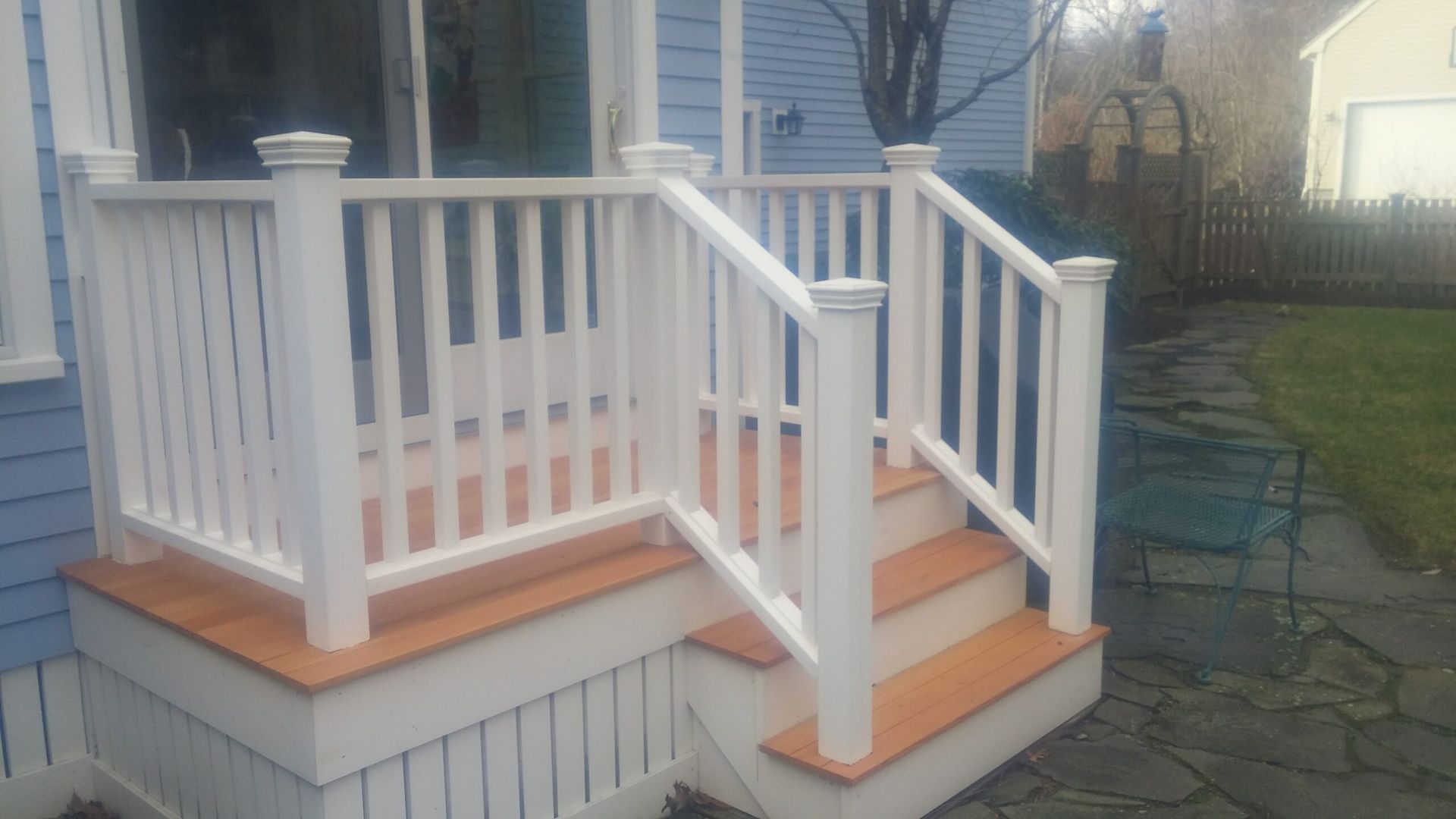 A white porch with wooden steps and railing on a blue house.