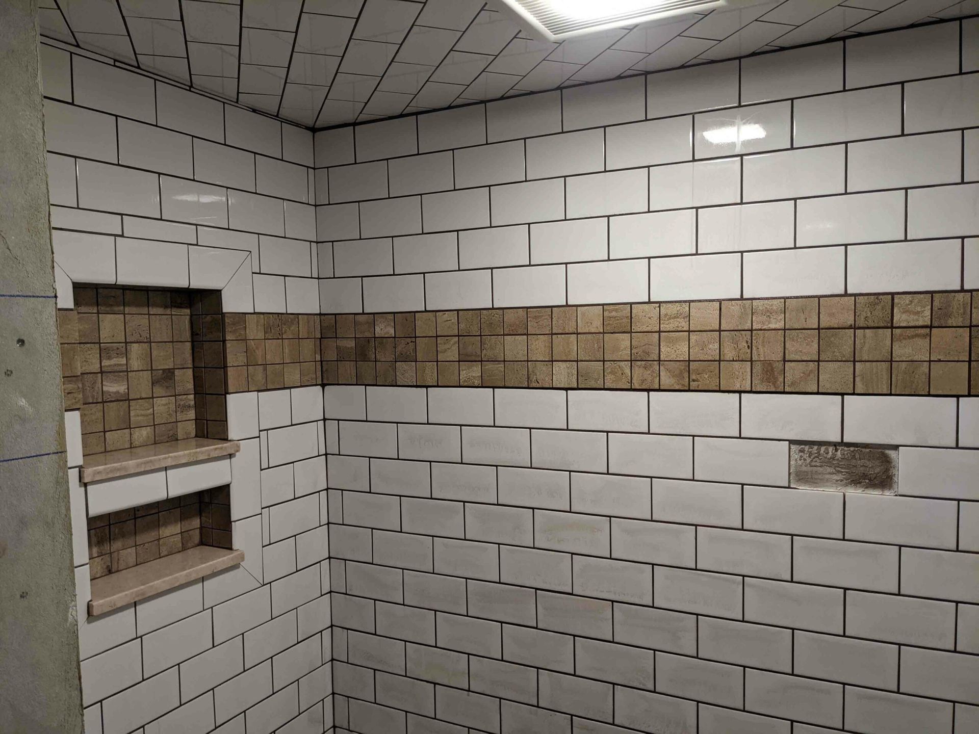 A bathroom with white tiles and brown tiles on the walls.