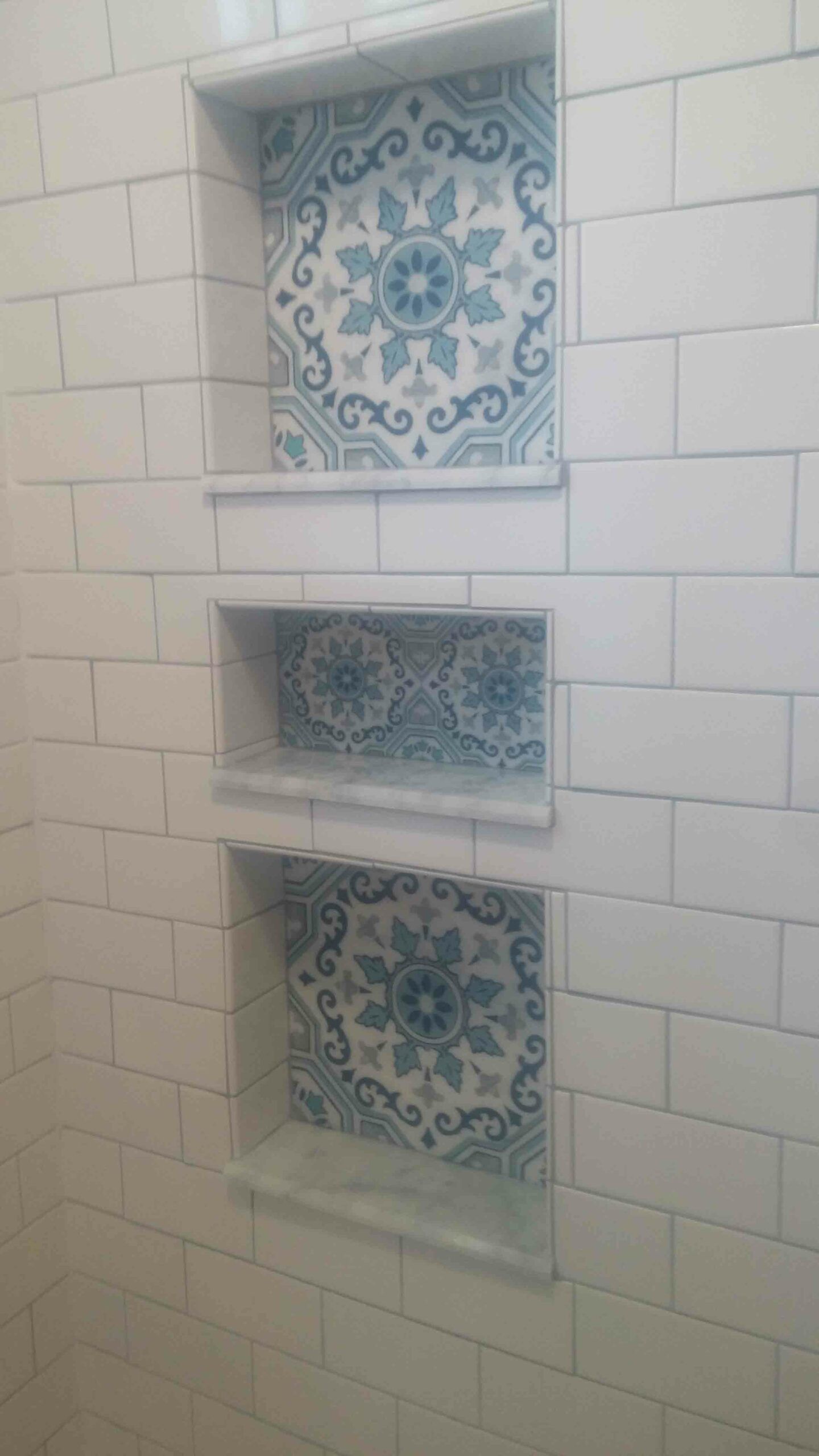 There are three shelves in the shower with blue and white tiles.