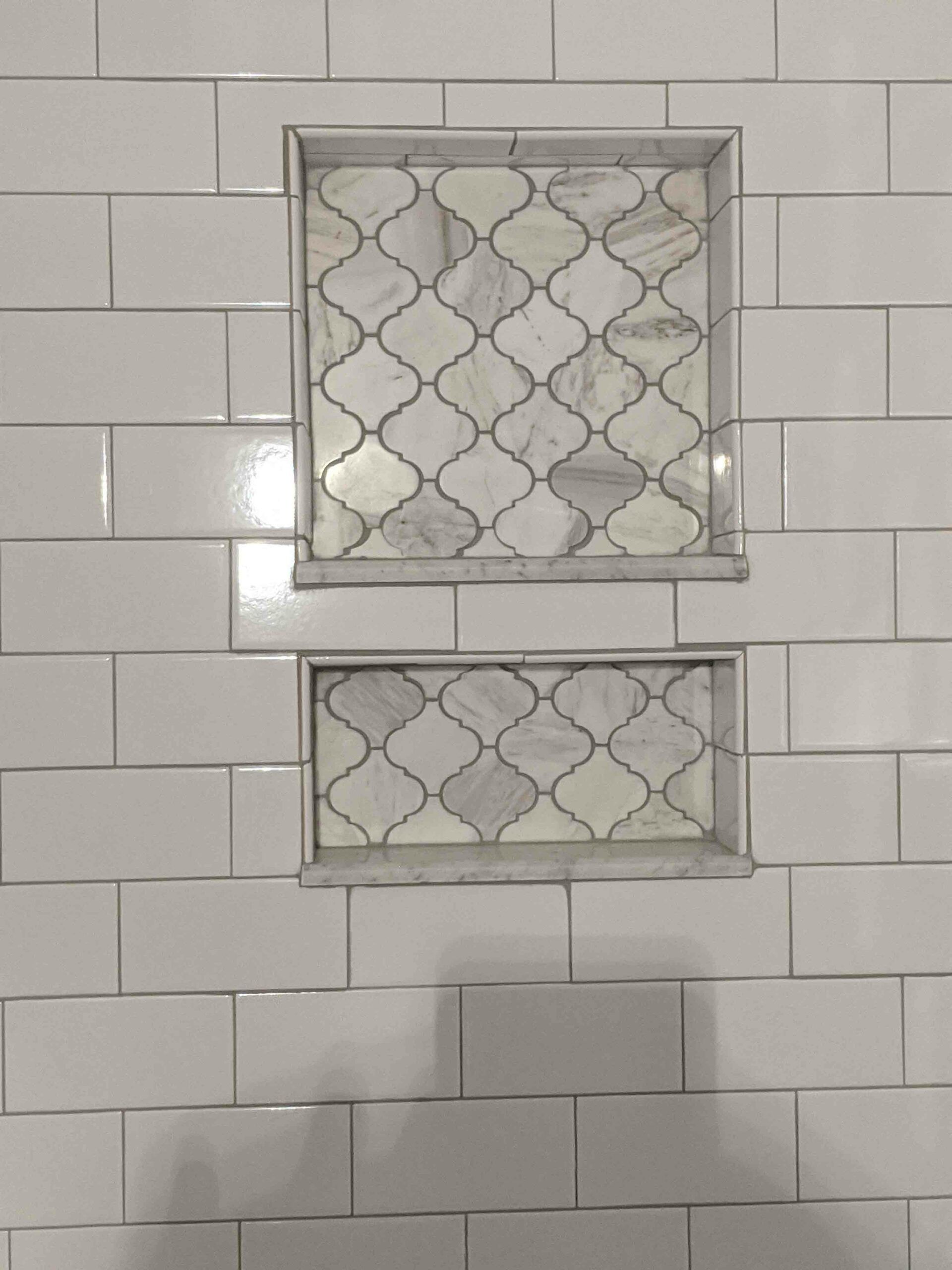 A bathroom wall with white tiles and two shower niches.