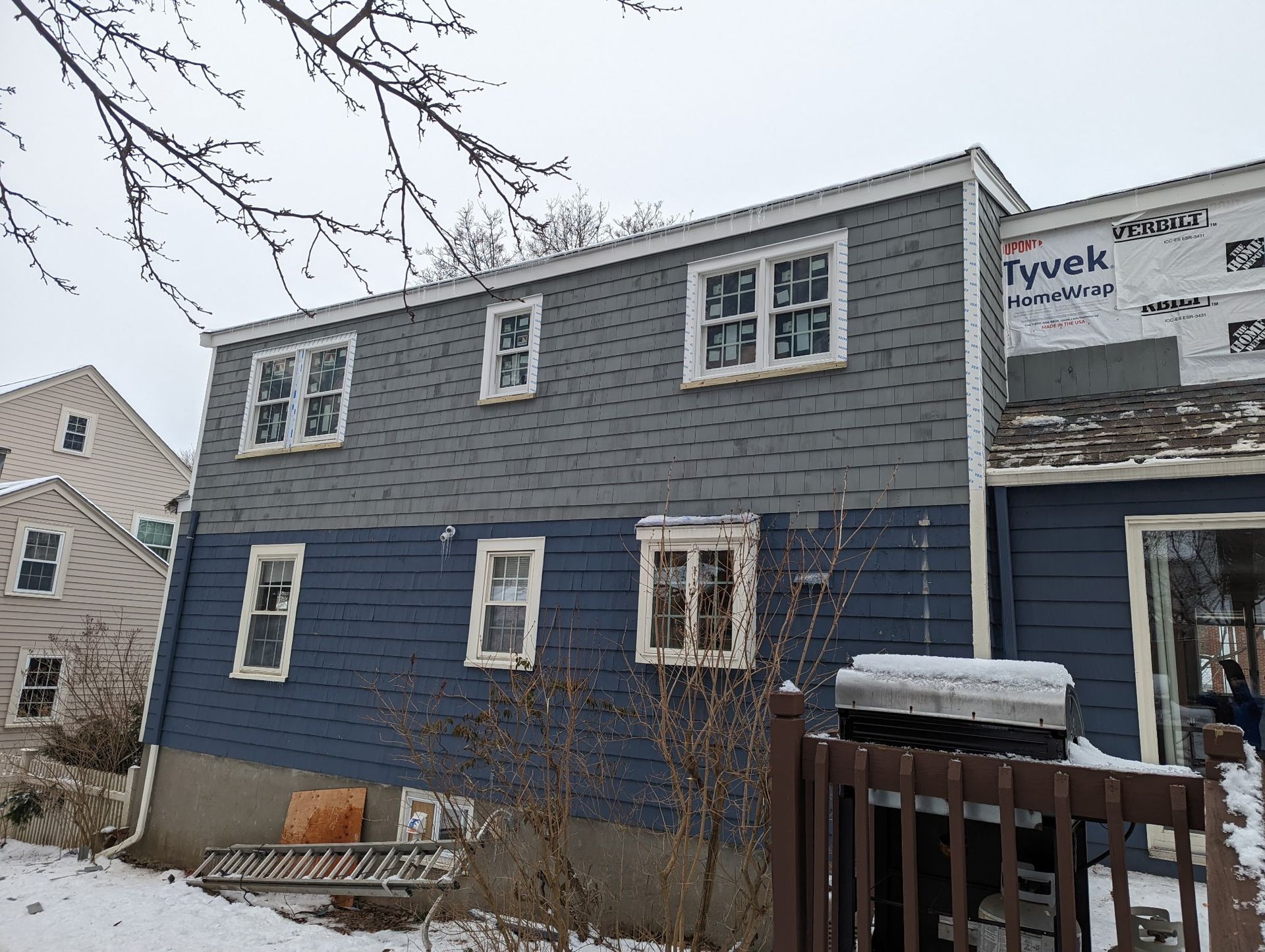 A blue house with a lot of windows is covered in snow.