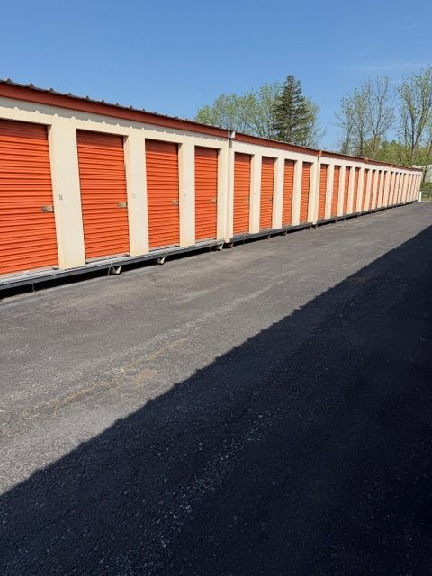 Row of orange storage unit doors along a long paved drive on a sunny day
