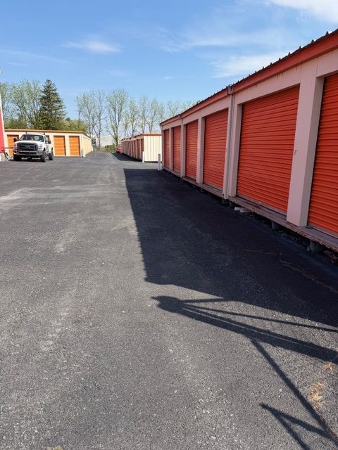 Storage unit row with orange doors along a paved lane on a sunny day
