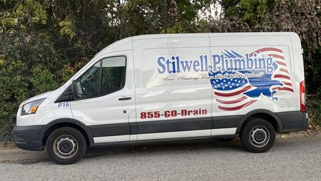White Stilwell Plumbing van with American flag graphic parked outdoors.