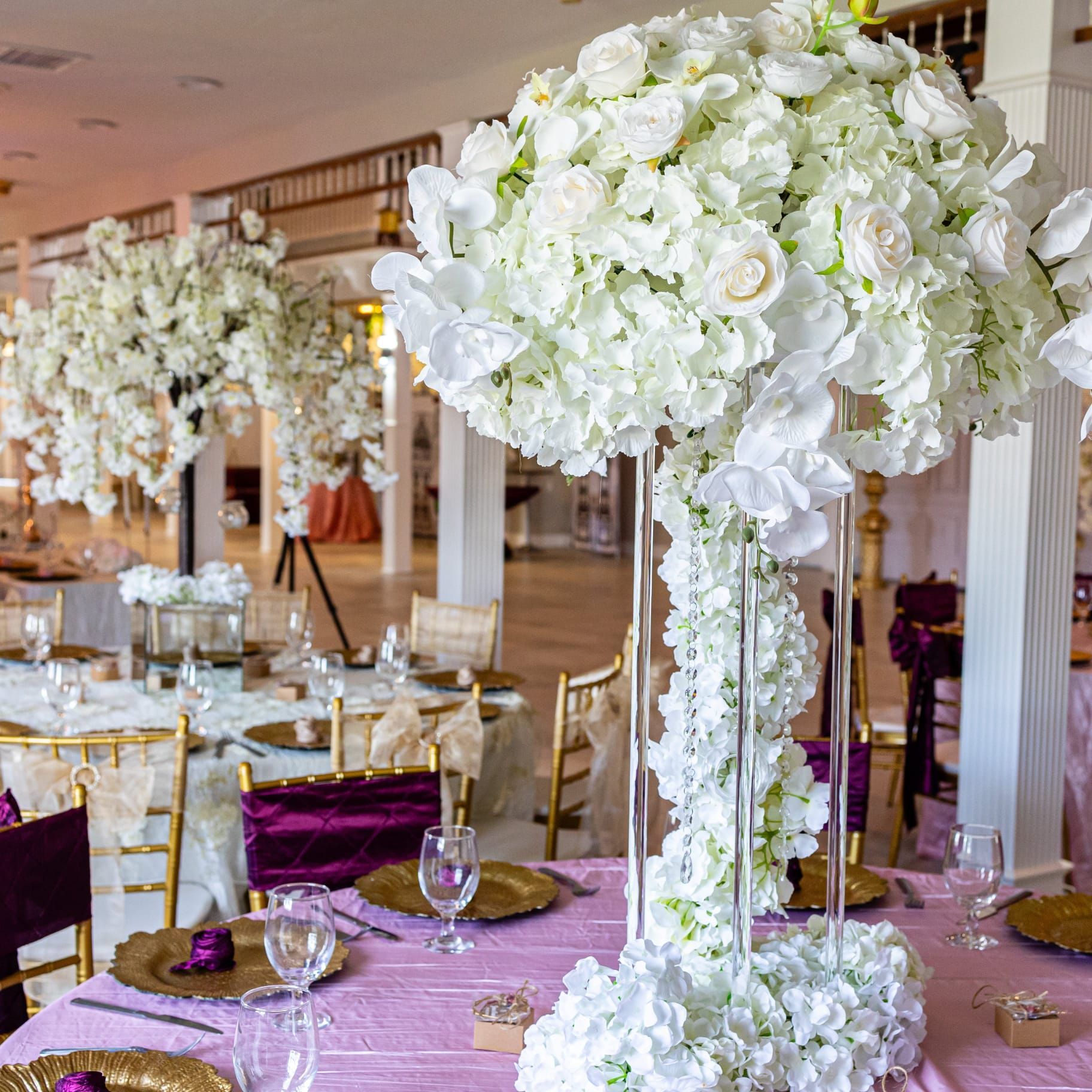 Elegant reception hall with white floral centerpieces on pink tablecloths.