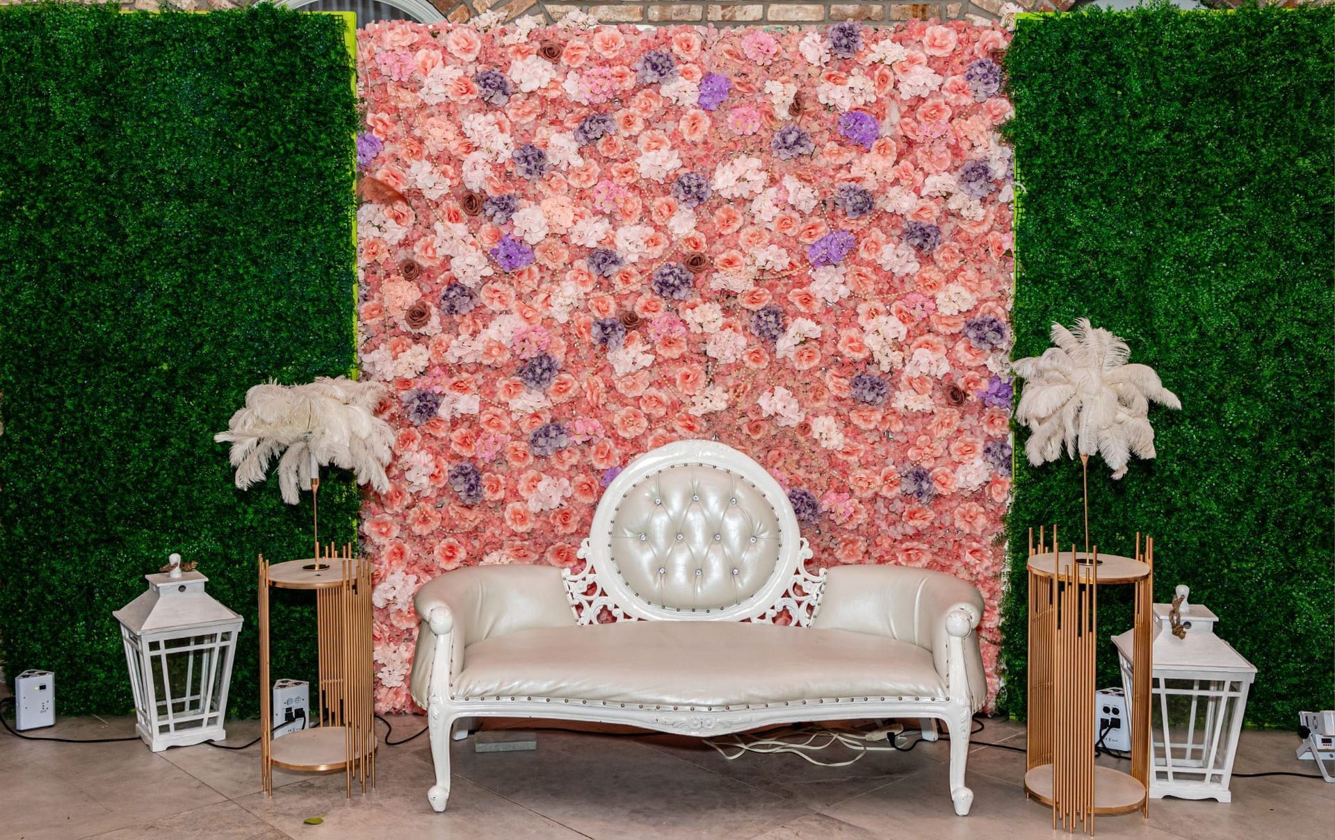 Flower wall backdrop with a white loveseat and decorative elements.
