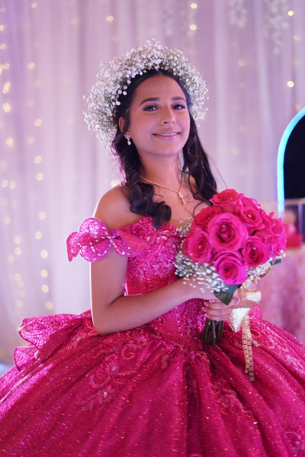 Woman in magenta ball gown holding roses, wearing flower crown, smiling.