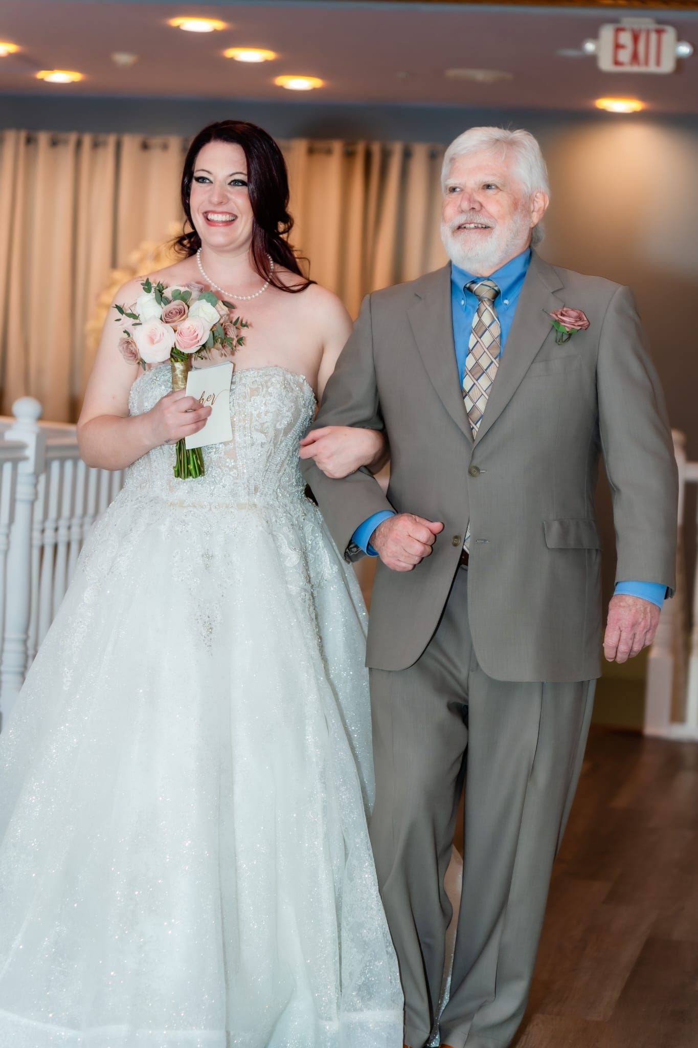 Bride in a sparkling white gown walks down the aisle arm-in-arm with a man in a gray suit, smiling.
