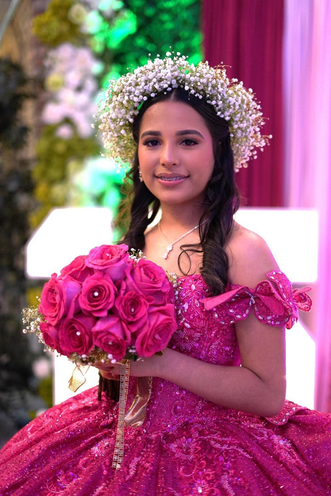 Young person in a pink sequined ball gown holds a bouquet of pink roses, wearing a flower crown, smiling.