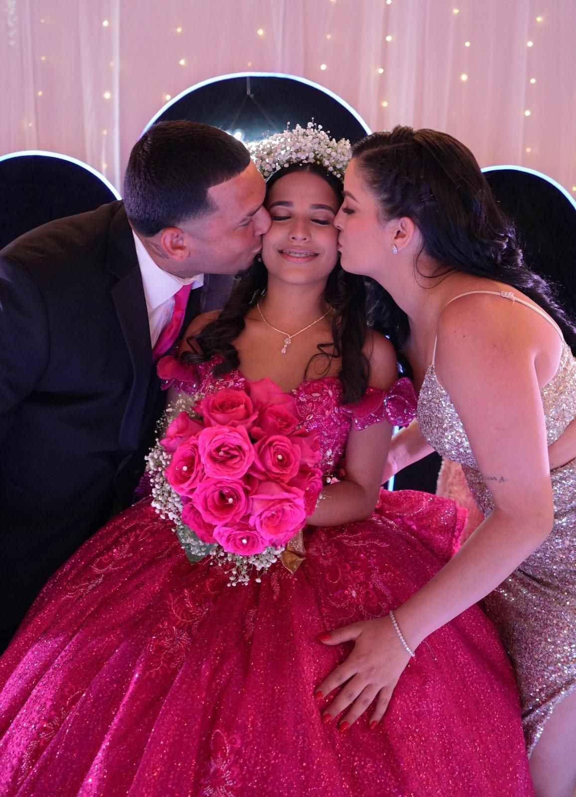Girl in fuchsia dress, tiara, holding roses, kissed by a man and woman. Illuminated background.