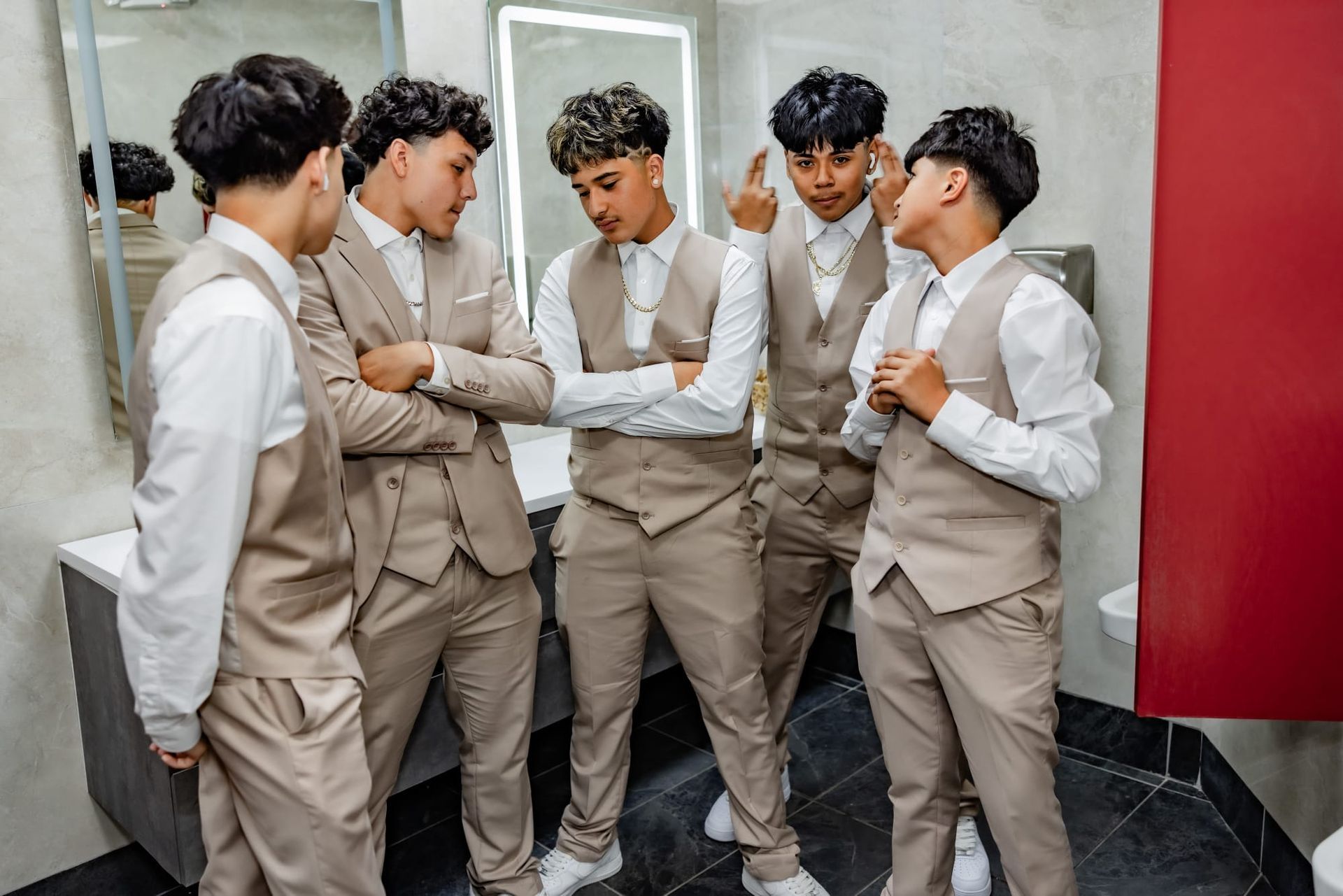 Five people in beige suits in a bathroom, some gesturing and talking.