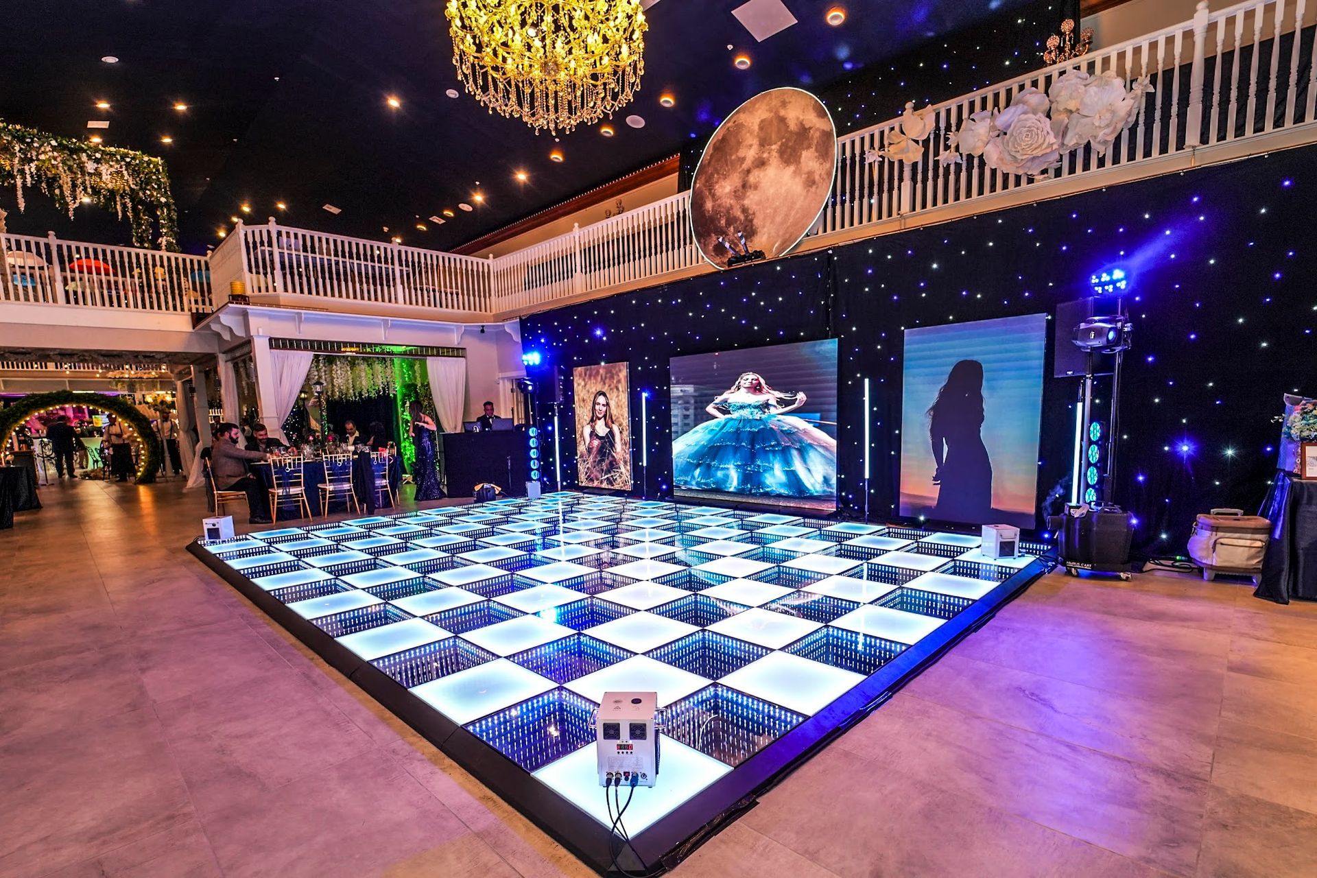 Light-up dance floor in a decorated venue with a large moon and stage backdrop.