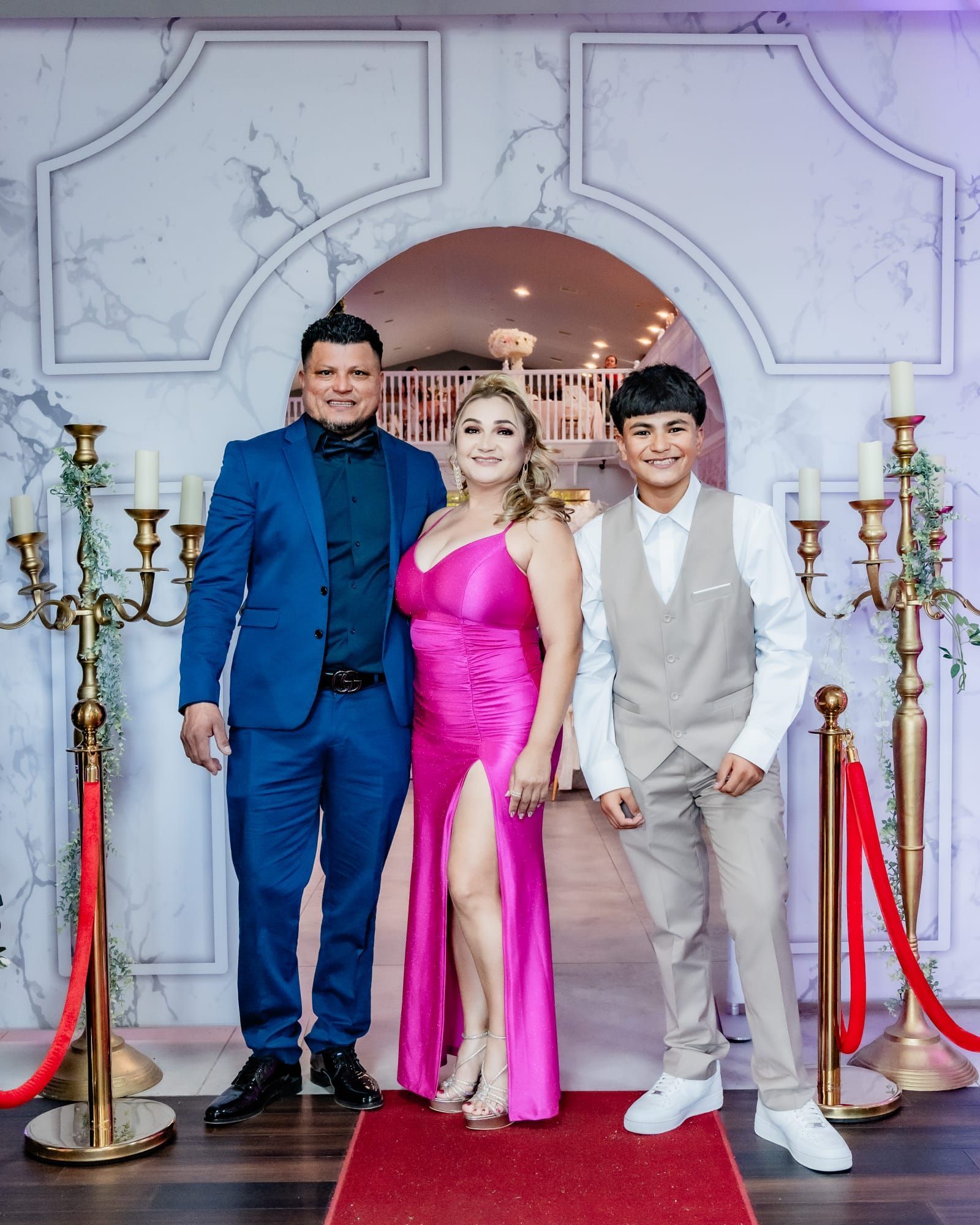 Family poses for a photo near a red carpet, with gold candelabras, under an archway.
