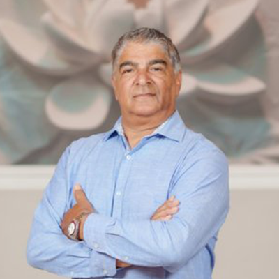 Man in blue shirt with arms crossed, standing in front of an abstract floral backdrop.