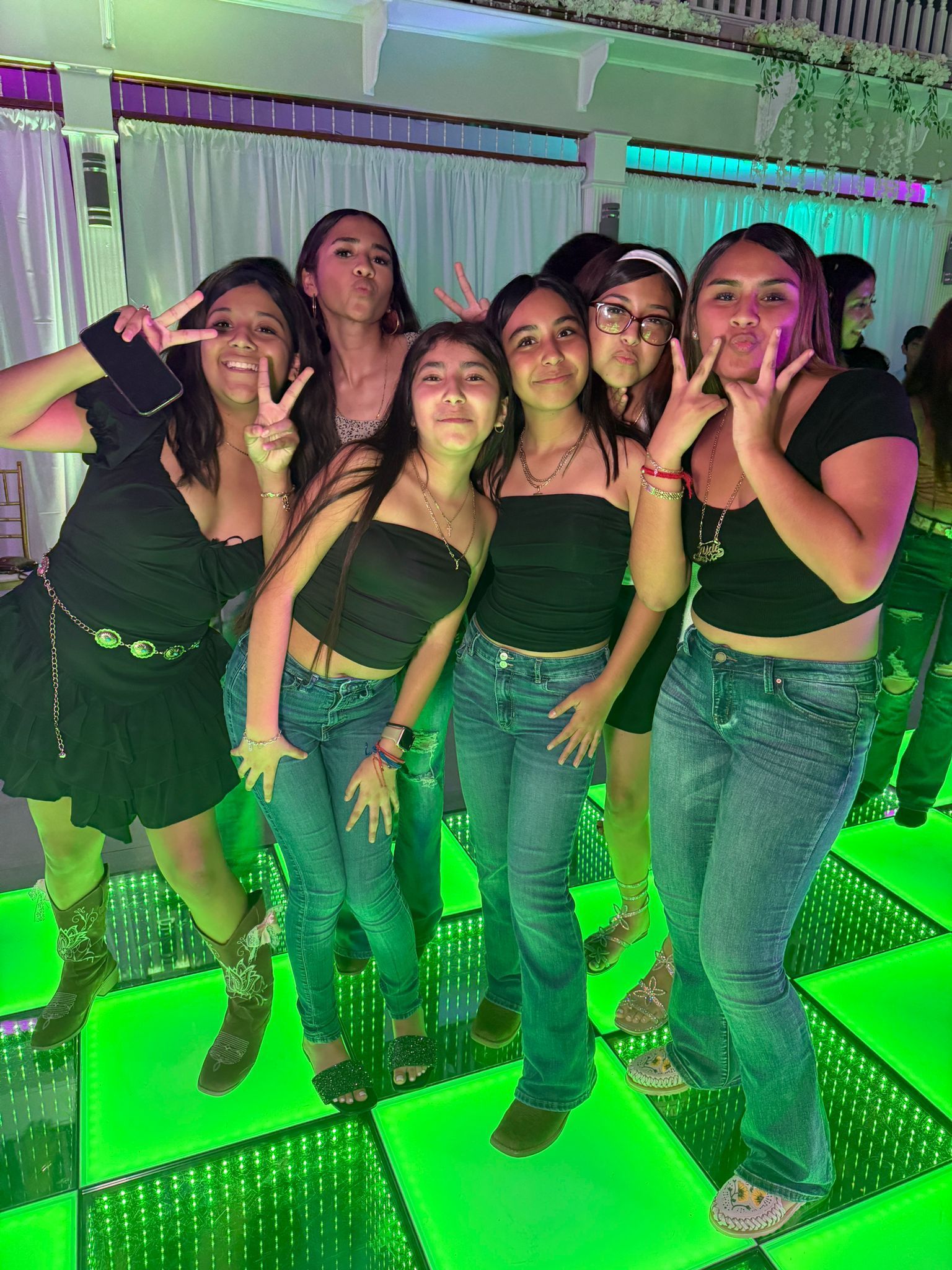 Group of friends posing on a green-lit dance floor, making peace signs and smiles.