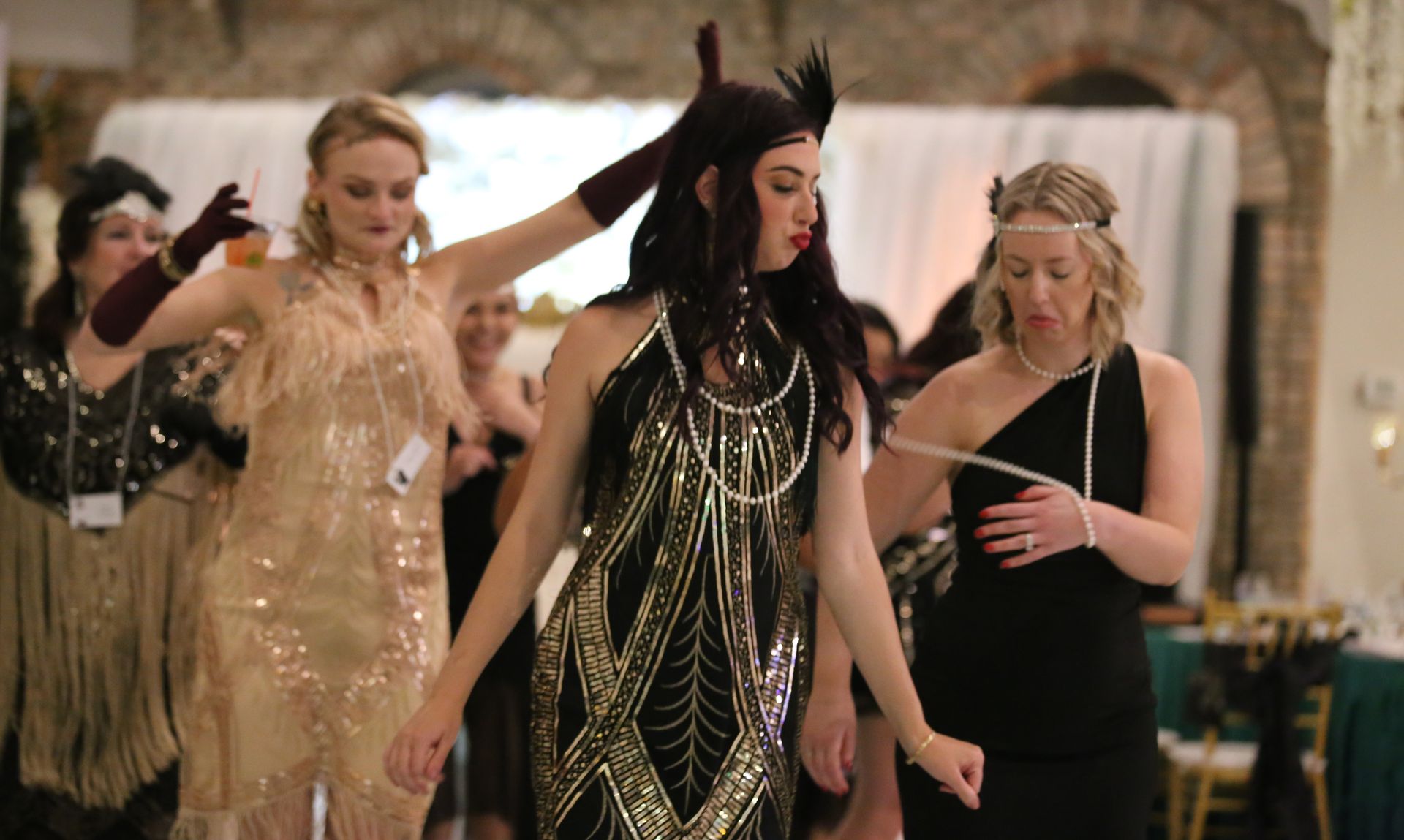 Women in flapper dresses dancing at a party, inside a decorated hall.