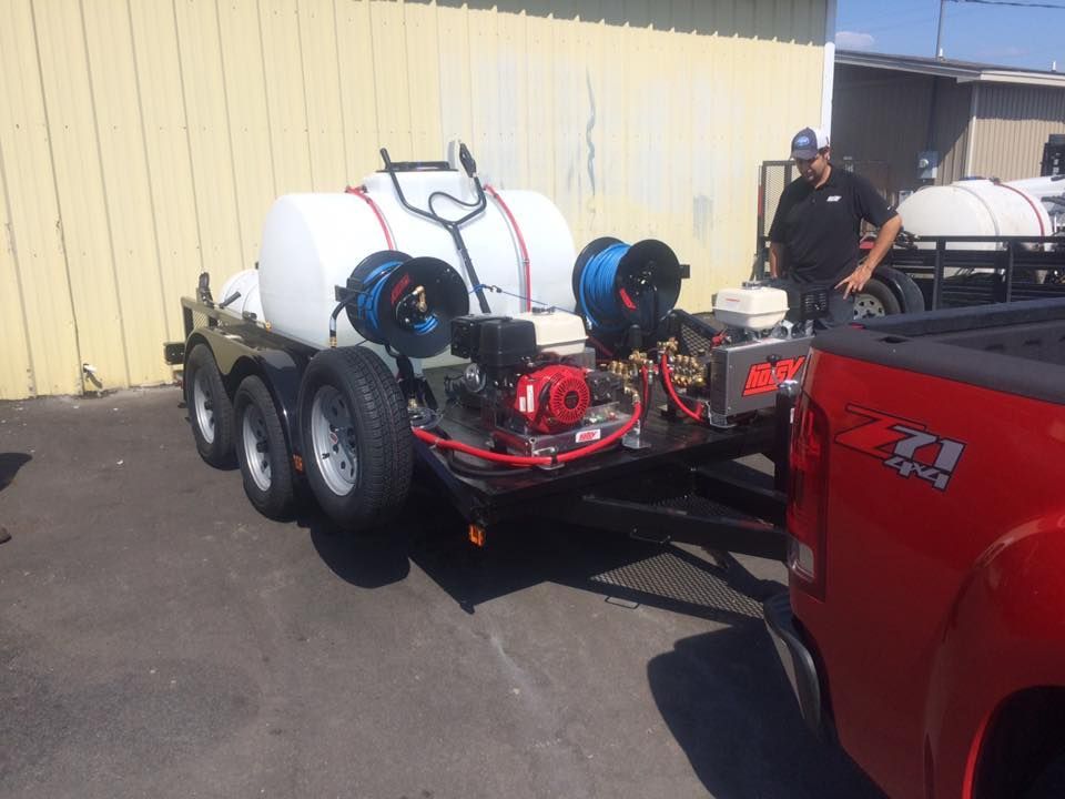 A man is standing next to a red truck with a trailer attached to it.