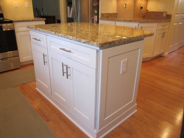 White kitchen island with granite countertop, doors, drawers, and an electrical outlet.