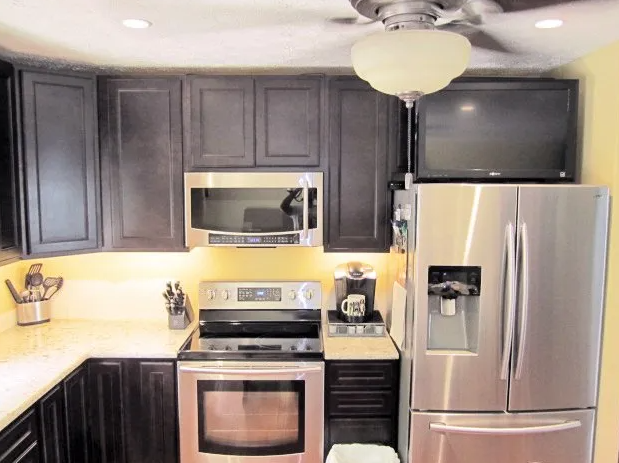 Kitchen with dark cabinets, stainless steel appliances, and a mounted TV above the refrigerator.