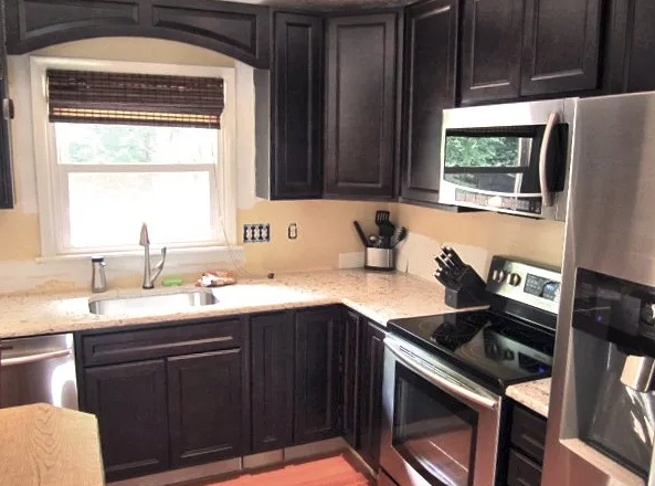 Dark brown kitchen cabinets, stainless steel appliances, off-white countertops, bamboo window shade.