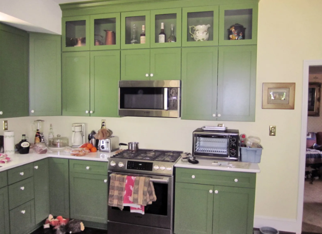 Green kitchen cabinets with stainless steel appliances against yellow walls.