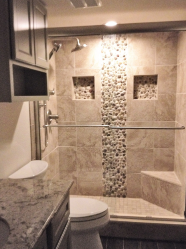 Shower with beige tiles, pebble accent, two recessed shelves, and a built-in bench.