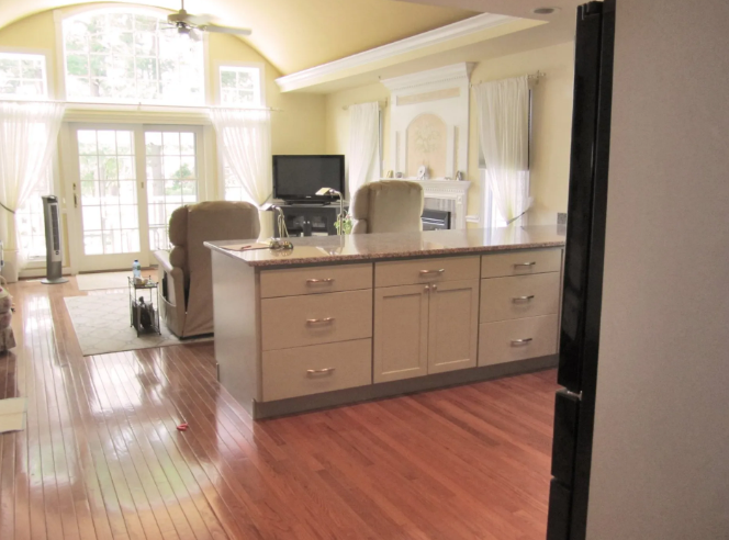 Spacious kitchen with a large island, hardwood floors, and a fireplace, featuring a TV and natural light.