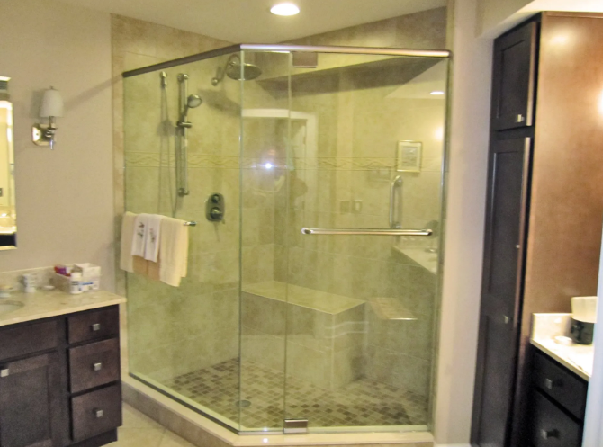 Corner shower with glass doors, stone tile walls and bench, dark cabinets, and fixtures.