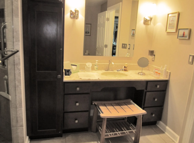 Bathroom vanity with dark cabinets, a light-colored countertop, and a wooden stool.
