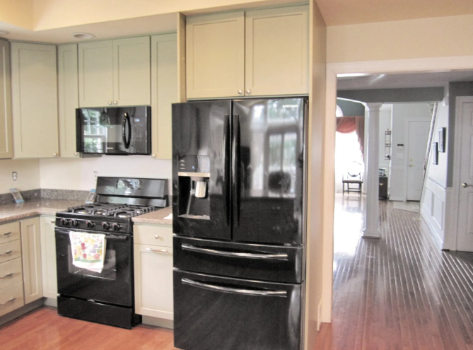 Kitchen with black appliances, light green cabinets, and hardwood floors.